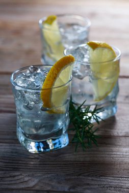 Limonlu cin, ardıç ve eski ahşap bir masada buz. Limon dilimli alkol içeceği ve eski ahşap bir masada ardıç dalı..