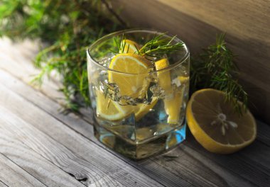 Mavi cin, tonik ve limonlu kokteyl. Buzlu alkollü içecek, limon dilimleri ve eski ahşap bir masada ardıç dalı..