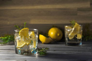 Mavi cin, tonik ve limonlu kokteyl. Buzlu alkollü içecek, limon dilimleri ve eski ahşap bir masada ardıç dalı..