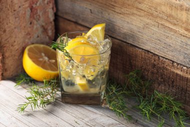 Mavi cin, tonik ve limonlu kokteyl. Buzlu alkollü içecek, limon dilimleri ve eski ahşap bir masada ardıç dalı..