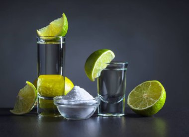 Tekila, limon dilimleri ve koyu arkaplanda tuz..