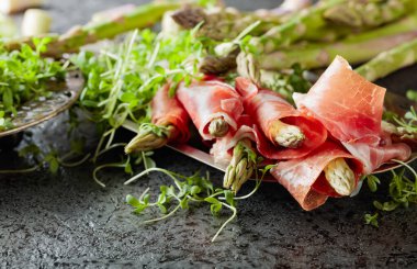 Prosciuttoya sarılı kuşkonmaz ve gri arka planda tere salatası..