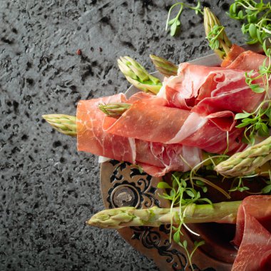 Prosciuttoya sarılı kuşkonmaz ve gri arka planda tere salatası. Üst görünüm, metin için boşluk kopyala. 