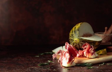 Prosciutto ve biberiyeli sulu kavun eski kahverengi bir masada. Boşluğu kopyala.