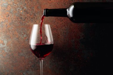 Kırmızı şarap bir şişeden paslı kahverengi arka plandaki bir şarap bardağına dökülür. Metnin için alanı olan ön görünüm.