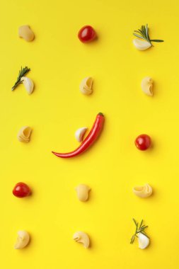 Sarı arka planda biber, sarımsak, domates ve biberiyeli makarna, yukarıdan görüş..