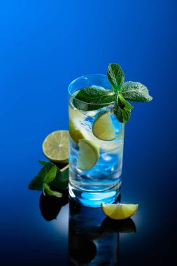 Buzlu, limonlu mojito kokteyli ve siyah yansıtıcı arka planda naneli..