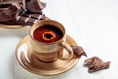 Beyaz ahşap bir masada sıcak çikolata ve kırık çikolata parçaları. Bir damla içki bardağa düşer. Boşluğu kopyala.