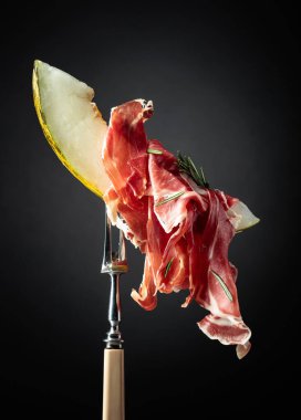 Prosciutto ve biberiyeli kavun. Kopyalama alanı olan siyah arkaplan.