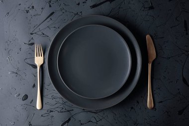 Siyah arka planda boş bir siyah plaka, çatal ve bıçak. Üst görünüm, alanı kopyala.