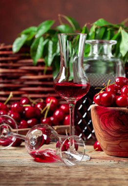 Bahçedeki bir masada, ahşap bir kasede kiraz likörü ve kirazlar. Arka planda yeşil yapraklar olan çit..