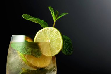 Limon dilimleri ve naneli soğuk bir içecek. Siyah zemin üzerinde Mojito olan dondurulmuş cam.. 