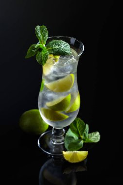 Buzlu, limonlu mojito kokteyli ve siyah yansıtıcı arka planda naneli..