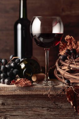 Eski ahşap bir masada üzümlü bir bardak ve bir şişe kırmızı şarap..