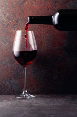 Kırmızı şarap bir şişeden paslı kahverengi arka plandaki bir şarap bardağına dökülür. Metnin için alanı olan ön görünüm.