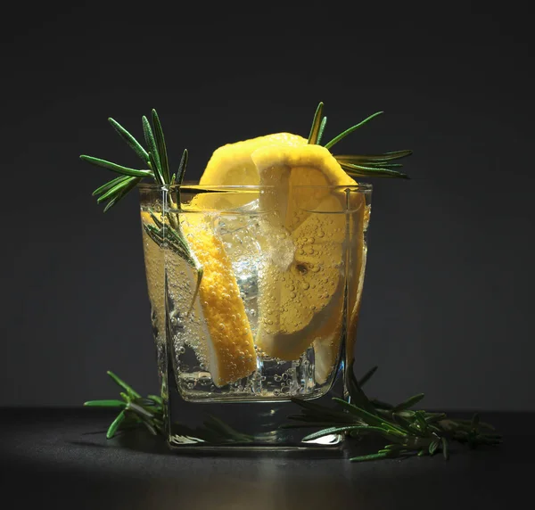 Cold carbonated drink with lemon and rosemary on a black table.