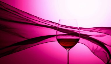 Sallanan saten perdenin arkasında bir kadeh kırmızı şarap. Mor arka plan.