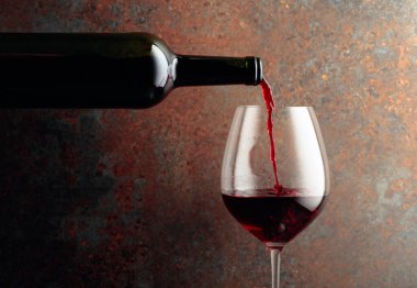 Kırmızı şarap bir şişeden paslı kahverengi arka plandaki bir şarap bardağına dökülür. Metnin için alanı olan ön görünüm.