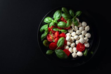 Domatesli Caprese salatası, mini mozzarella ve siyah tabakta fesleğen. İtalyan yemeği ve sağlıklı vejetaryen diyeti. Boşluğu kopyala, üst görünüm.