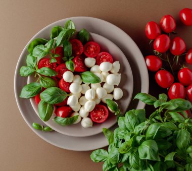 Domatesli Caprese salatası, kahverengi arka planda mini mozzarella ve fesleğen. İtalyan yemeği ve sağlıklı vejetaryen diyeti. Boşluğu kopyala, üst görünüm.