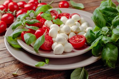 Domatesli Caprese salatası, eski ahşap bir masada mini mozzarella ve fesleğen. İtalyan yemeği ve sağlıklı vejetaryen diyeti.