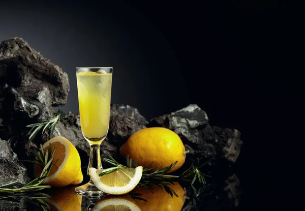 伝統的な自家製レモンリキュールのリモンチェッロと黒の反射的背景に新鮮な柑橘類 レモンスライスとローズマリーの枝を持つイタリアの伝統的なリキュールのリモンチェッロ — ストック写真