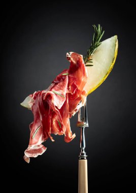 Prosciutto ve biberiyeli kavun. Kopyalama alanı olan siyah arkaplan.