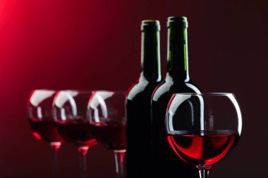 Siyah arka planda kırmızı şarap şişeleri ve bardaklar. Boşluğu kopyala.