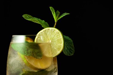 Limon dilimleri ve naneli soğuk bir içecek. Siyah zemin üzerinde Mojito olan dondurulmuş cam.. 