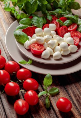 Domatesli Caprese salatası, eski ahşap bir masada mini mozzarella ve fesleğen. İtalyan yemeği ve sağlıklı vejetaryen diyeti.