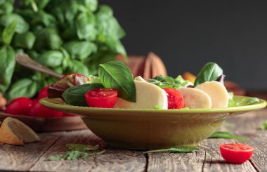 Eski ahşap bir masada yeşil tabakta mozarella, domates ve fesleğen ile yeşil salata.  