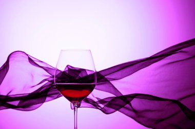 Sallanan saten perdenin arkasında bir kadeh kırmızı şarap. Mor arka plan.