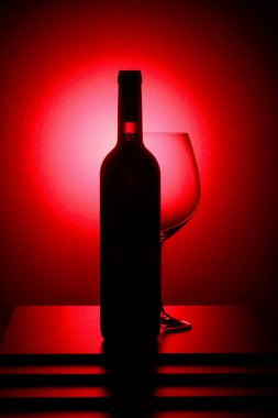 Bir şişe kırmızı şarap ve boş bir bardak. Kırmızı arka ışık.