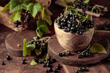 Kahverengi bir masada, ahşap bir kabın içinde, olgun, siyah bir kuş üzümü..