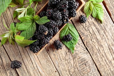 Eski ahşap bir masanın üzerinde yaprakları olan böğürtlenler. Üst görünüm.