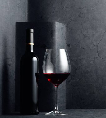 Siyah taş bir masanın üzerinde kırmızı şarap şişesi ve bardak..