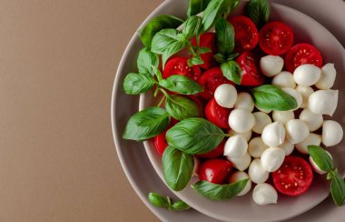 Domatesli Caprese salatası, kahverengi arka planda mini mozzarella ve fesleğen. İtalyan yemeği ve sağlıklı vejetaryen diyeti. Boşluğu kopyala, üst görünüm.