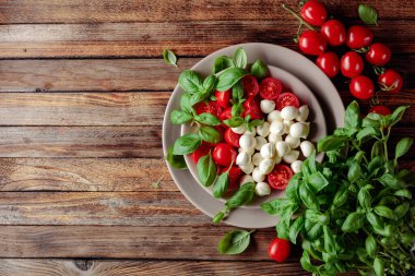 Domatesli Caprese salatası, eski ahşap bir masada mini mozzarella ve fesleğen. İtalyan yemeği ve sağlıklı vejetaryen diyeti.