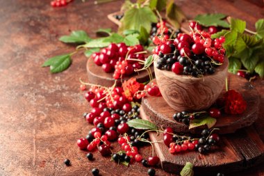 Mutfak masasında vişne, kırmızı ve siyah frenk üzümü. Yapraklarla sulu meyveler.