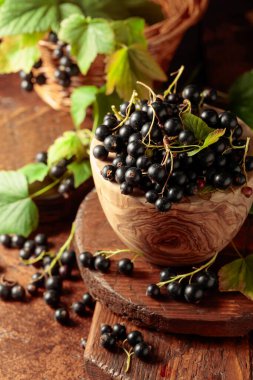 Kahverengi bir masada, ahşap bir kabın içinde, olgun, siyah bir kuş üzümü..