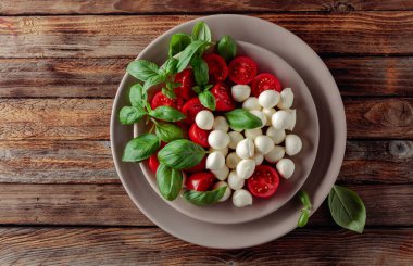 Domatesli Caprese salatası, eski ahşap bir masada mini mozzarella ve fesleğen. İtalyan yemeği ve sağlıklı vejetaryen diyeti.