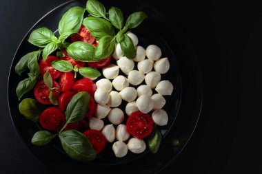 Domatesli Caprese salatası, mini mozzarella ve siyah tabakta fesleğen. İtalyan yemeği ve sağlıklı vejetaryen diyeti. Boşluğu kopyala, üst görünüm.