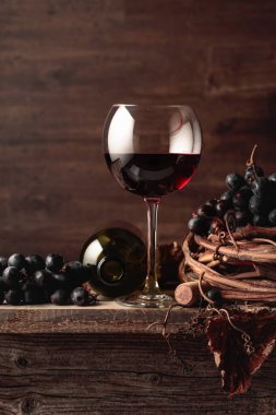 Eski ahşap bir masada üzümlü bir bardak ve bir şişe kırmızı şarap..
