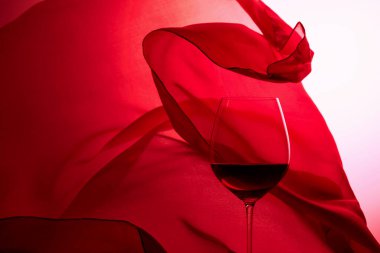 Kırmızı saten perdenin arkasında bir kadeh kırmızı şarap.