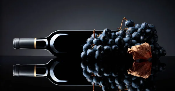 Botella Vino Tinto Racimo Uvas Sobre Fondo Negro Reflectante Enfoque —  Fotos de Stock