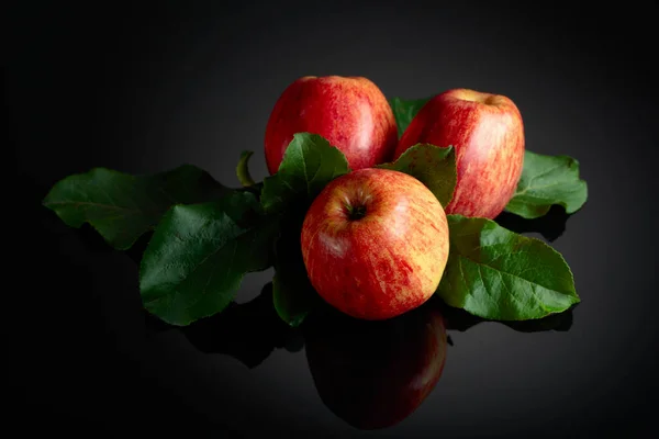 有叶子的多汁苹果 黑色反光背景的新鲜苹果 — 图库照片