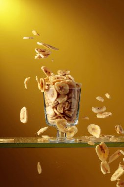 Muz cipsleri cam kaseye düşer. Kopyalama alanı olan sarı arkaplan.