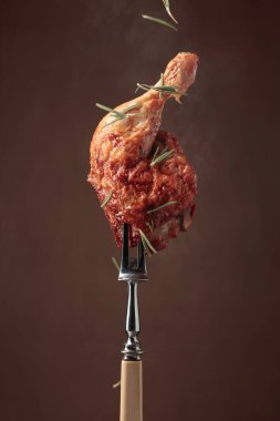 Koyu kahverengi arka planda biberiye serpilmiş ızgara tavuk bacağı. Çataldaki tavuk budu..