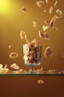 Muz cipsleri cam kaseye düşer. Kopyalama alanı olan sarı arkaplan.