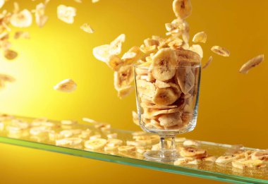 Muz cipsleri cam kaseye düşer. Kopyalama alanı olan sarı arkaplan.